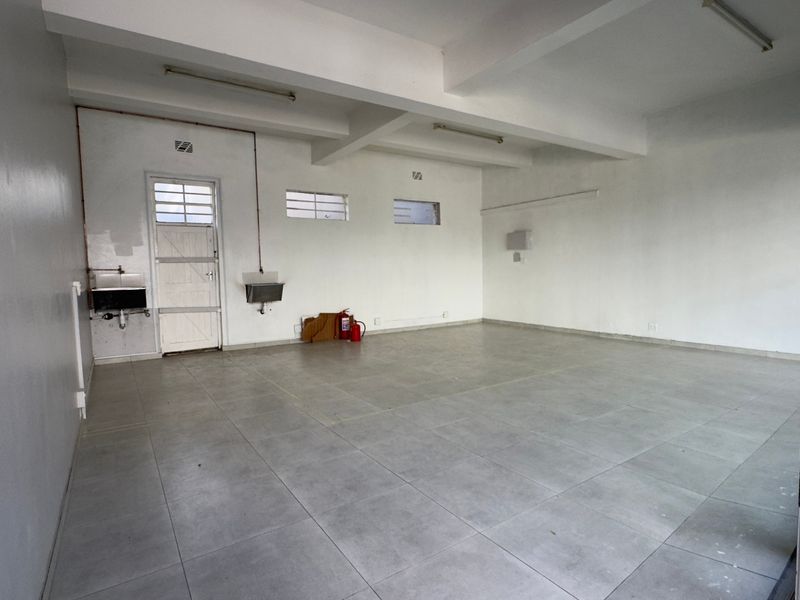 An empty, functional commercial kitchen space featuring tiled flooring, wall-mounted stainless steel sinks, and exposed utility piping, ready for custom fit-out.