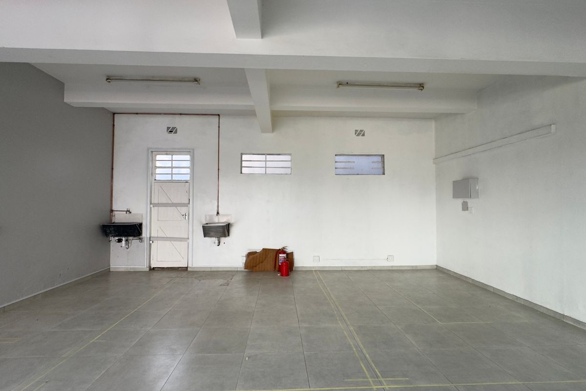 An empty, functional utility space featuring tiled flooring, exposed ceiling beams, wall-mounted sinks, and basic infrastructure suitable for commercial or service use.