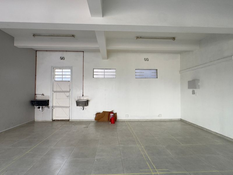 An empty, functional utility space featuring tiled flooring, exposed ceiling beams, wall-mounted sinks, and basic infrastructure suitable for commercial or service use.