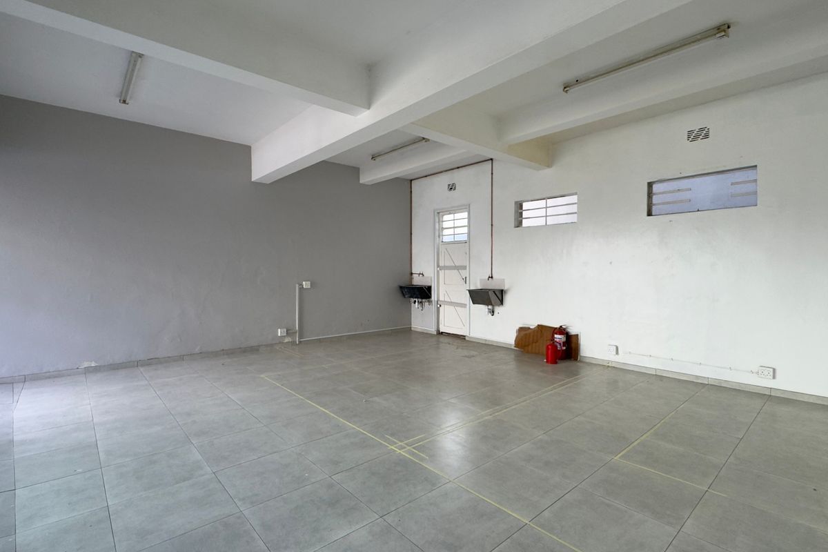 An empty, functional commercial kitchen space featuring tiled flooring, wall-mounted sinks, and exposed ceiling beams, ready for restaurant fit-out.