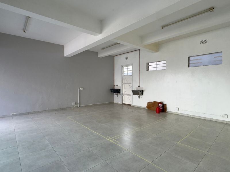 An empty, functional commercial kitchen space featuring tiled flooring, wall-mounted sinks, and exposed ceiling beams, ready for restaurant fit-out.