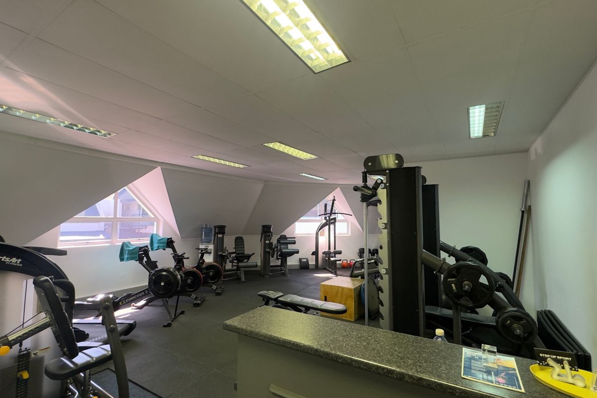 A functional gym space featuring rubberized flooring, recessed fluorescent lighting, and a built-in reception counter, situated under a pitched roof with natural light.