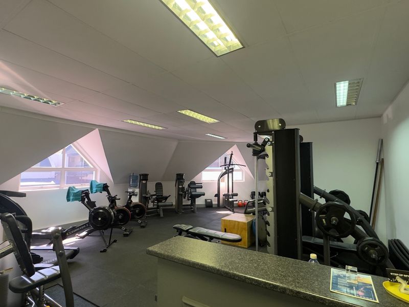 A functional gym space featuring rubberized flooring, recessed fluorescent lighting, and a built-in reception counter, situated under a pitched roof with natural light.
