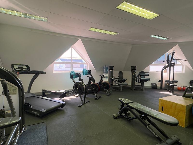 A well-equipped gym space featuring rubber flooring, recessed lighting, split-system air conditioning, and unique triangular windows providing natural light.