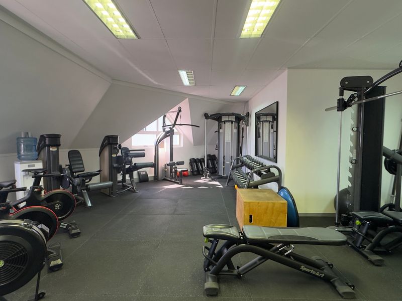 A well-equipped gym featuring rubber flooring, recessed lighting, and a mirrored wall, providing a functional space for fitness activities.