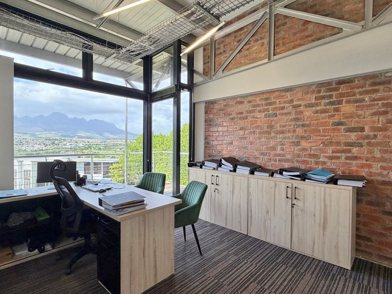 Modern office space featuring exposed brick walls, industrial steel trusses, and expansive windows offering scenic mountain views.