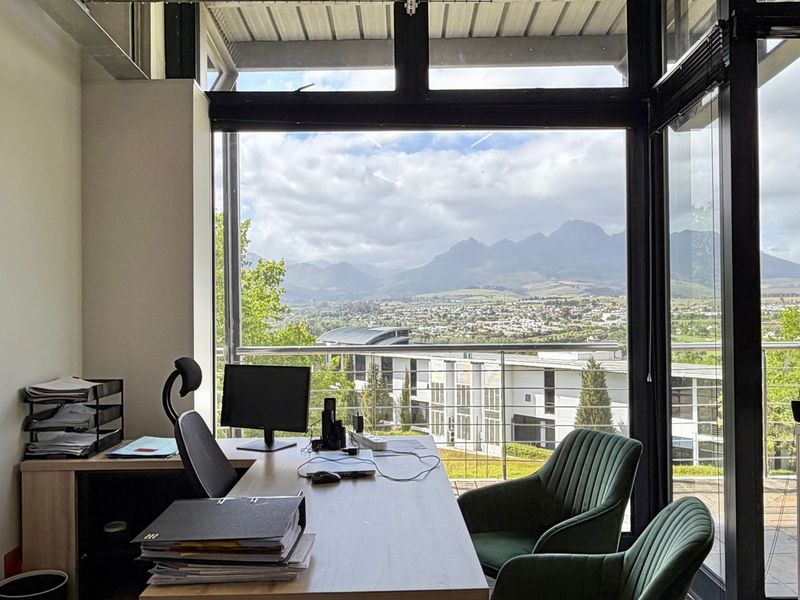Modern office space featuring floor-to-ceiling windows with expansive mountain and valley views, exposed brick accents, and an open, airy atmosphere.