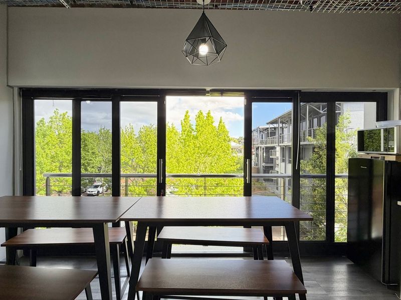 Modern open-plan office space featuring exposed brick accents, sleek black-framed sliding doors leading to a balcony, and contemporary pendant lighting.