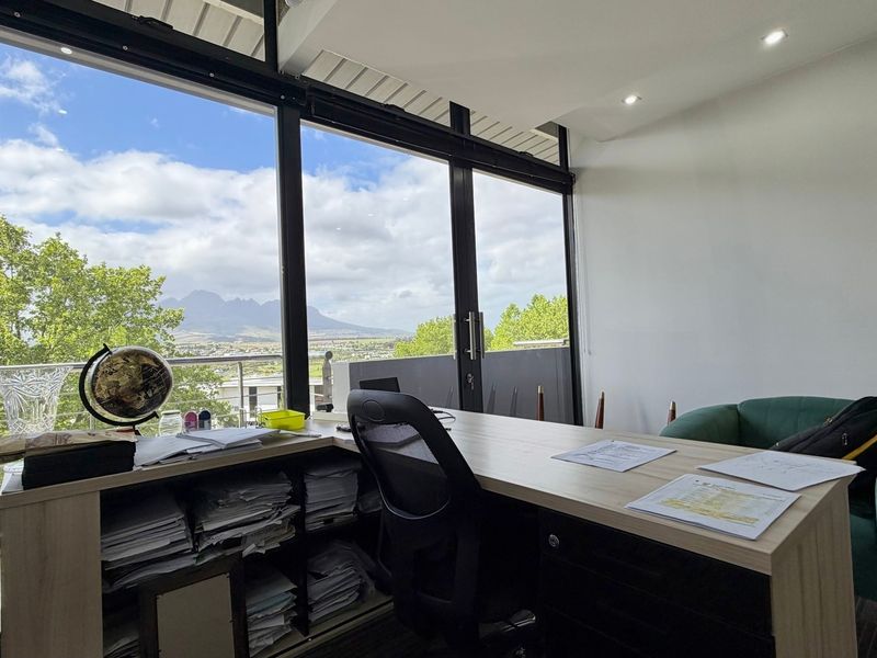 Bright office space featuring expansive floor-to-ceiling windows with scenic mountain views and direct access to a private balcony.