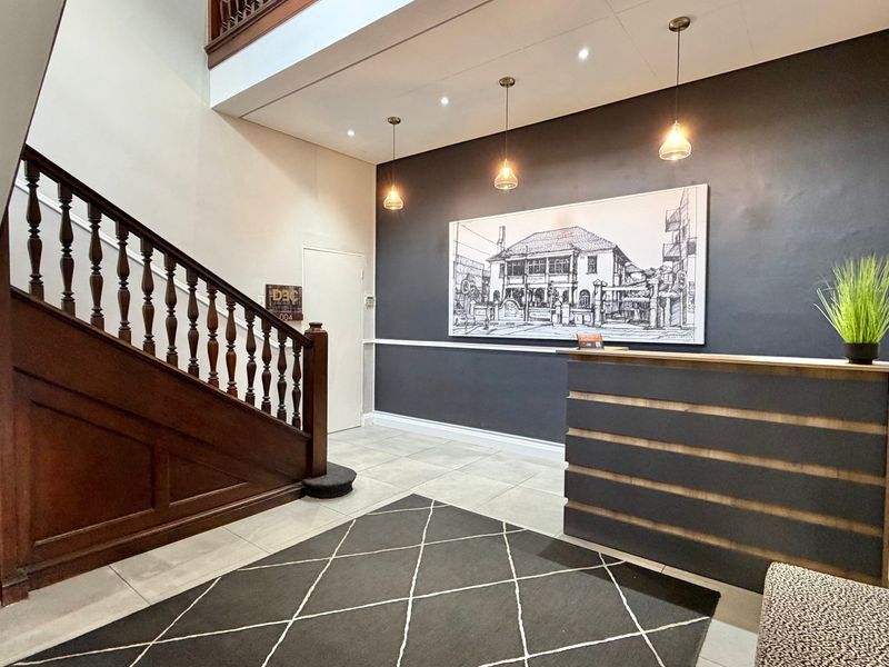 A professional office reception area featuring a classic wooden staircase, tiled flooring, and a modern reception desk with decorative pendant lighting.