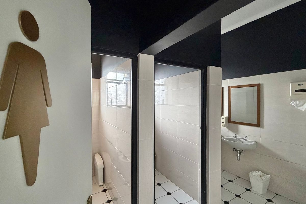 A clean, functional office restroom featuring tiled walls and floors, individual toilet cubicles, and a wall-mounted basin with a mirror.