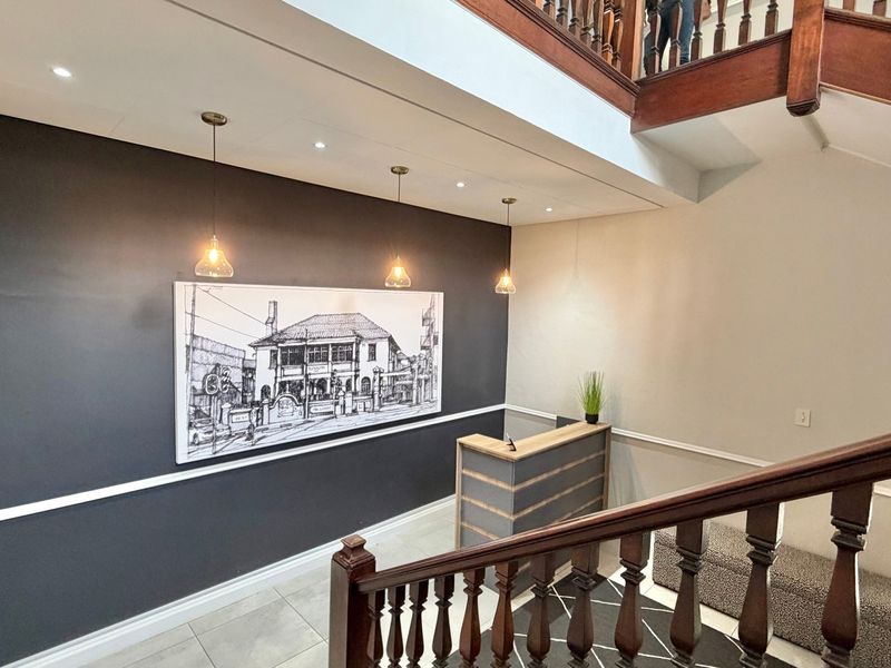 Welcoming office entrance featuring a classic wooden staircase with balustrade, tiled flooring, and modern pendant lighting against a dark feature wall.