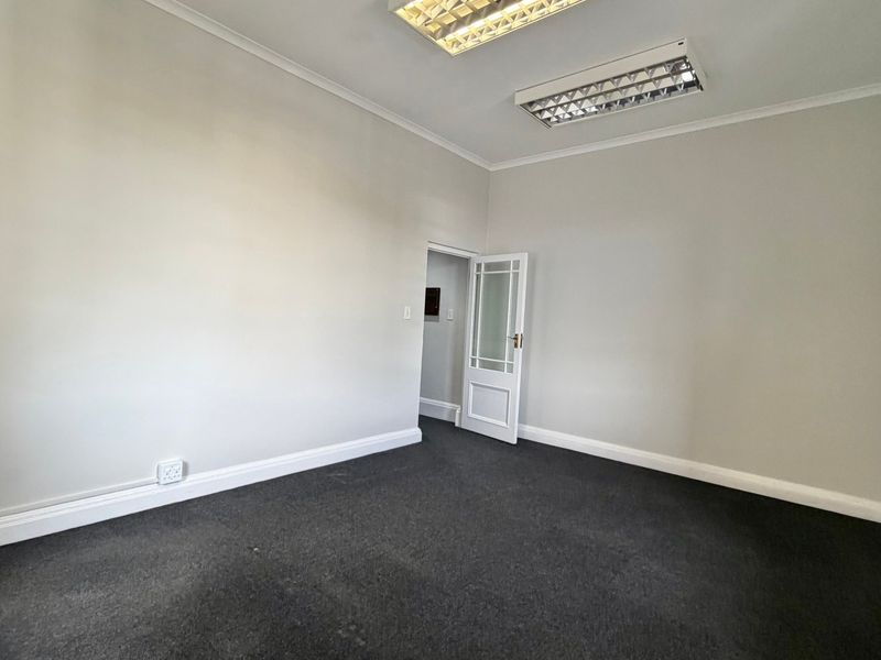 A clean, empty office space featuring neutral walls, dark carpeting, and functional overhead fluorescent lighting, suitable for a professional workspace.