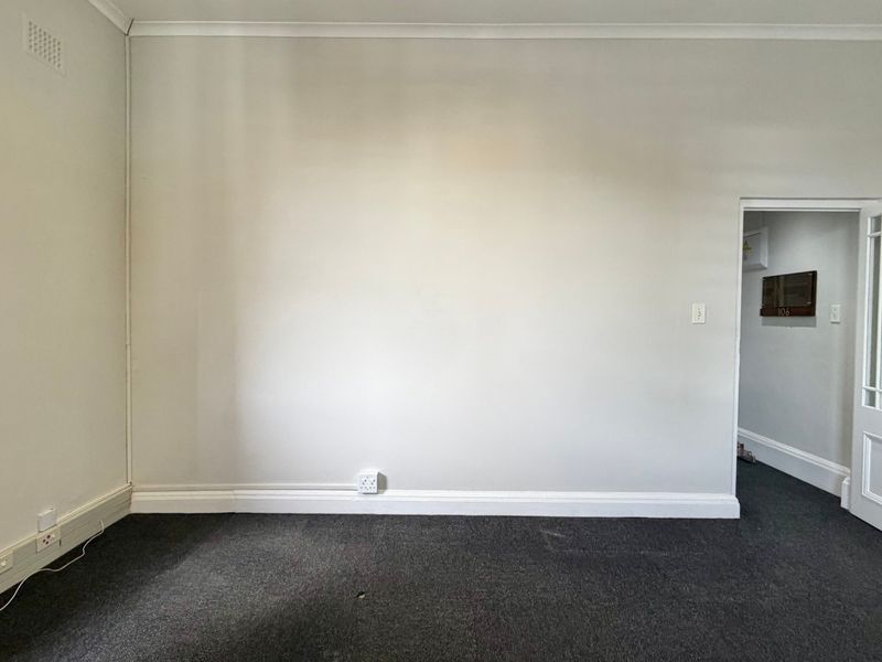 A vacant office space featuring neutral walls, dark carpet flooring, and a classic multi-pane glass door leading to the hallway.