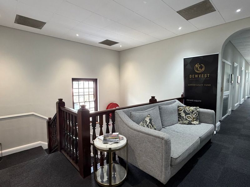 A well-maintained office hallway featuring a wooden staircase balustrade, recessed ceiling lighting, and a professional carpeted finish.