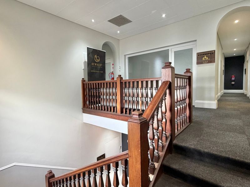 A well-maintained office building hallway featuring a classic wooden balustrade, carpeted stairs, and professional lighting.