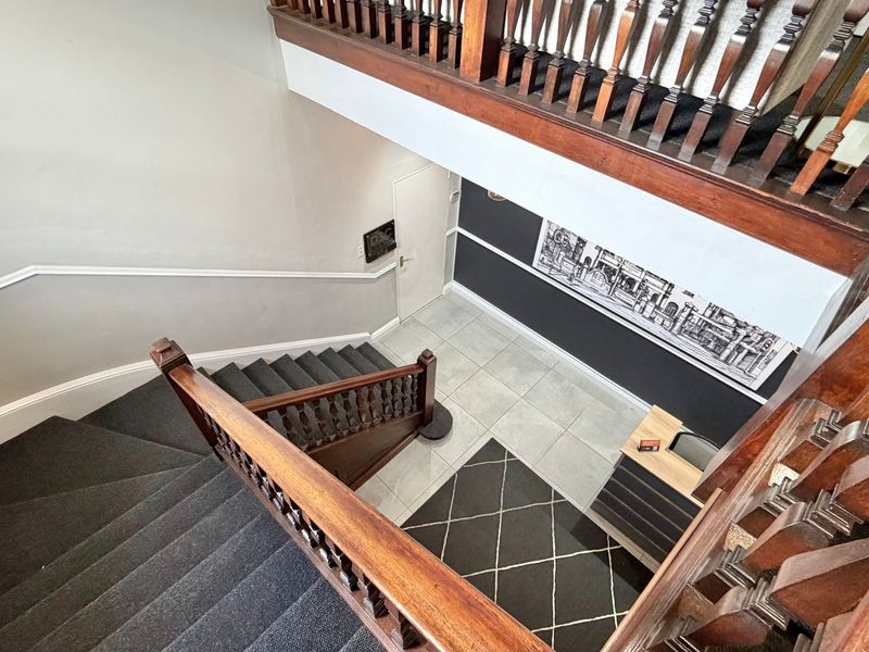 A high-angle view of an office building hallway featuring a classic wooden staircase with a detailed balustrade and clean tiled flooring.