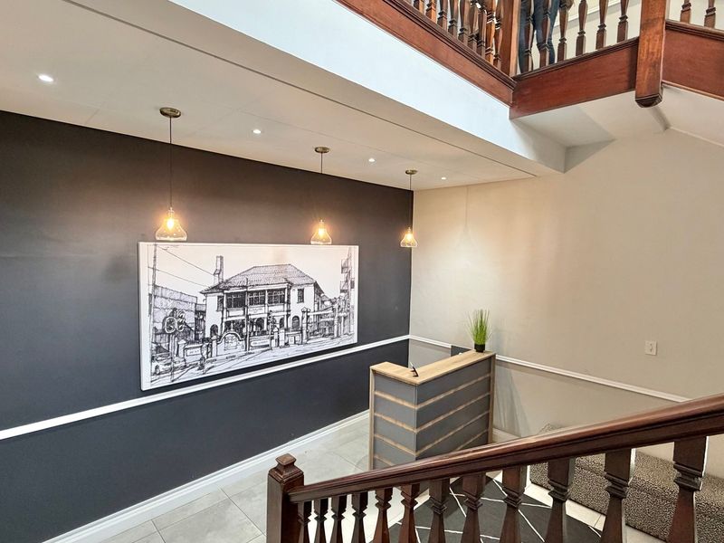 A welcoming office entrance featuring a wooden staircase with a classic balustrade, a reception desk, and modern pendant lighting against a dark accent wall.