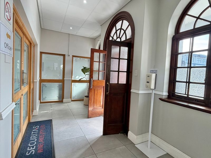 A bright and welcoming office entrance featuring tiled flooring, classic arched timber-framed windows, and elegant timber-framed glass doors.