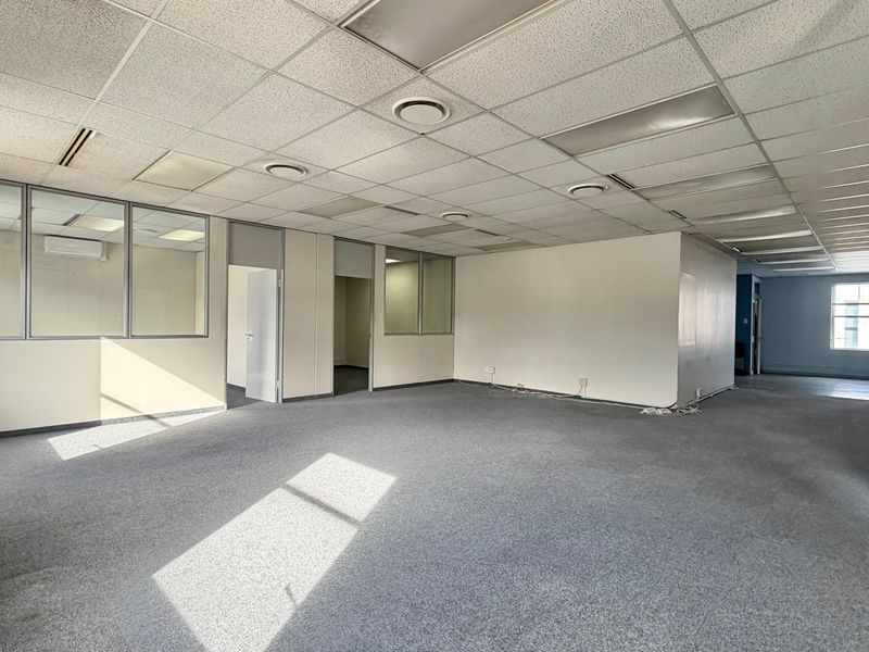 Spacious open-plan office area featuring suspended ceilings, glass partitions, and carpeted flooring, offering a versatile workspace layout.