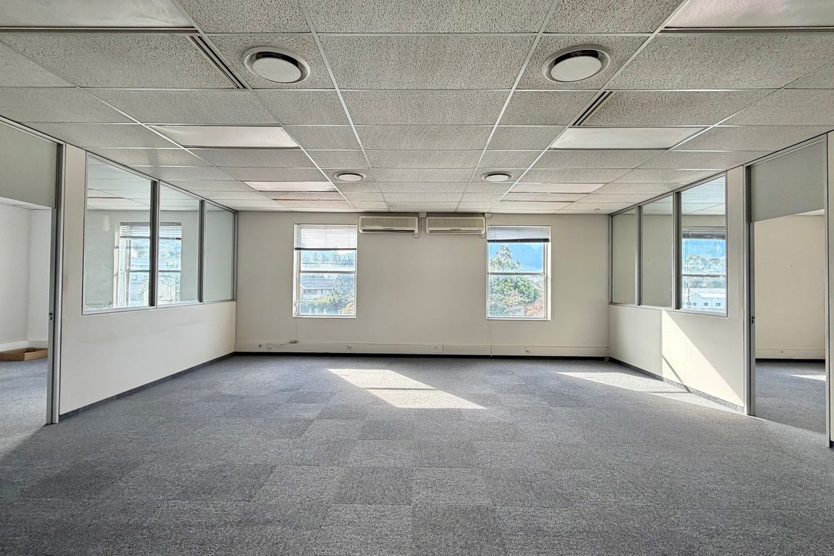 Spacious open-plan office area featuring suspended ceilings, recessed lighting, wall-mounted air conditioning units, and glass partitioning for a professional workspace environment.