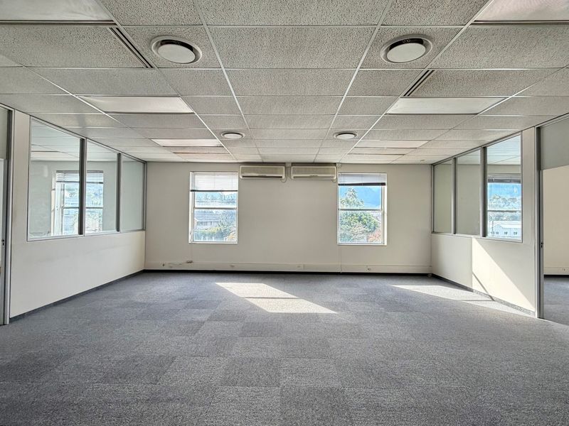 Spacious open-plan office area featuring suspended ceilings, recessed lighting, wall-mounted air conditioning units, and glass partitioning for a professional workspace environment.