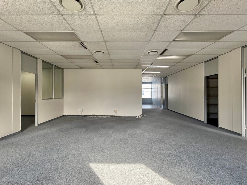 An open-plan office space featuring suspended ceilings, recessed lighting, and carpet tiles, offering a versatile layout for various business configurations.