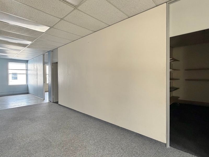 An empty office space featuring a suspended ceiling, recessed lighting, and an adjacent storage closet with built-in shelving.