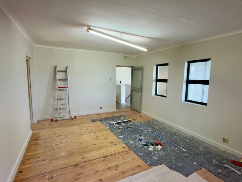 A bright, empty office space featuring polished timber flooring, modern aluminium window frames, and neutral wall finishes, currently undergoing minor finishing works.