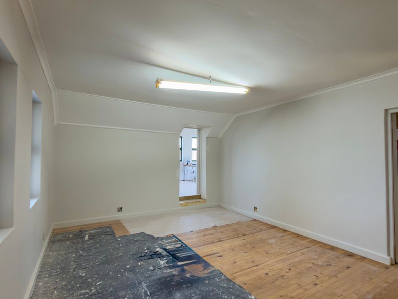 An empty office space featuring timber flooring, coved cornicing, and natural light from casement windows, currently undergoing renovation.