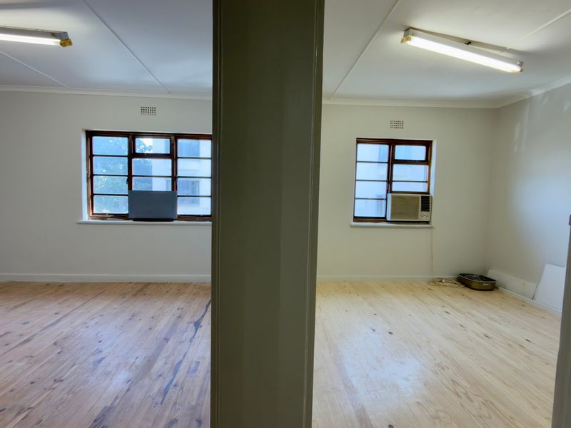 A vacant office space featuring timber flooring, fluorescent lighting, and a window-mounted air conditioning unit.