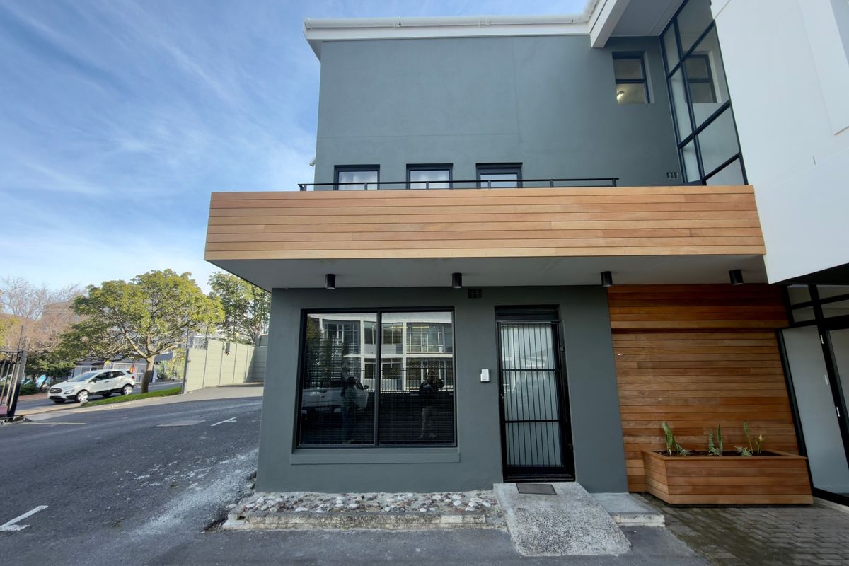 Modern office building exterior featuring contemporary grey facade, timber cladding accents, large windows, and a secure entrance with a concrete access ramp.