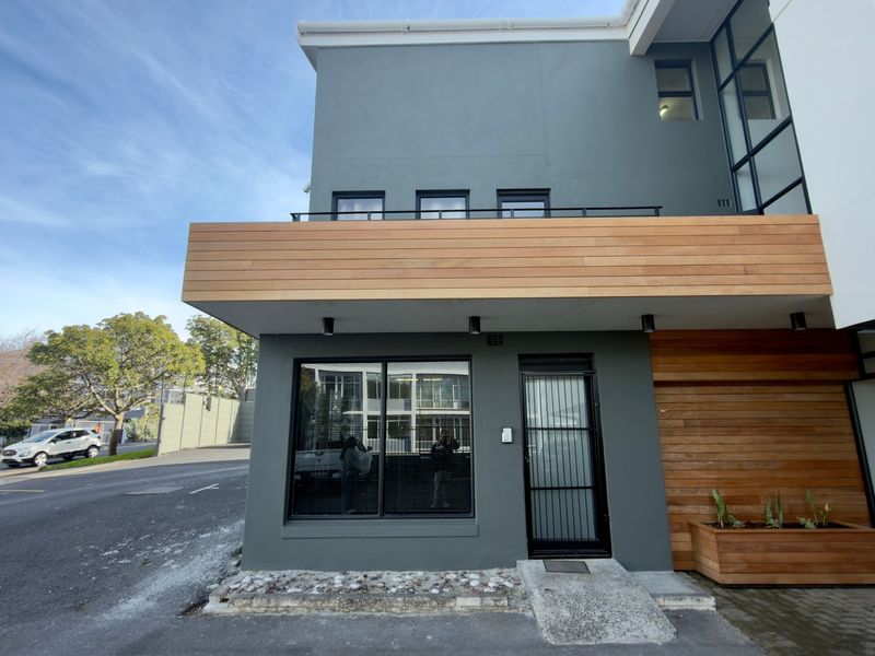 Modern office building exterior featuring contemporary grey facade, timber cladding accents, large windows, and a secure entrance with a concrete access ramp.
