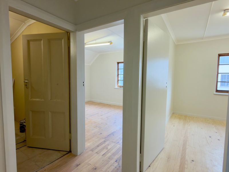 A bright hallway providing access to multiple office rooms, featuring polished timber flooring and neutral wall finishes throughout.