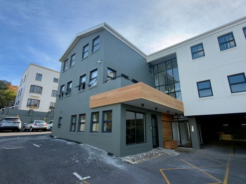 Modern multi-story office building exterior featuring a combination of grey and white facade finishes, timber accents, and an integrated ground-level parking area.