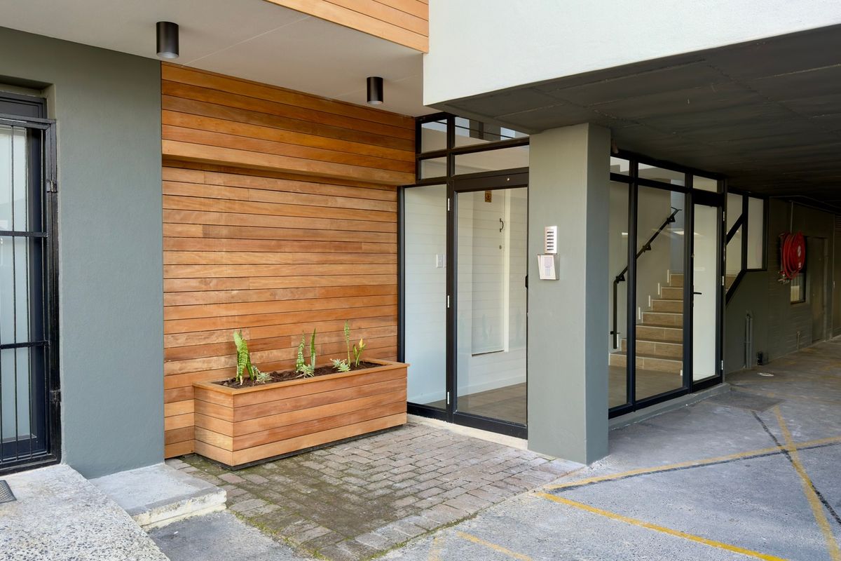 Modern office building entrance featuring timber cladding, glass doors, and a paved walkway leading to an internal staircase.