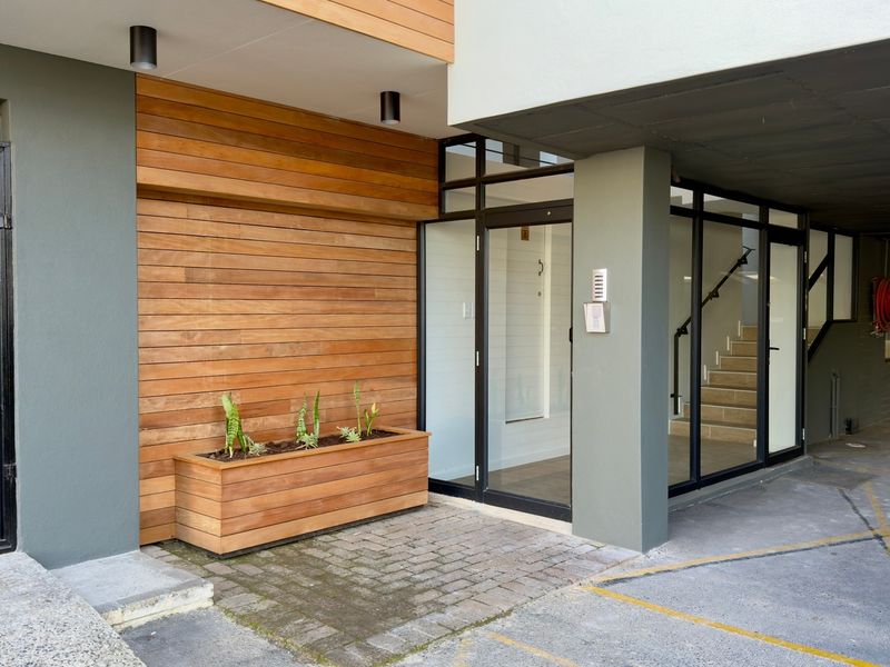 Modern office building entrance featuring timber cladding, glass doors, and a paved walkway leading to an internal staircase.