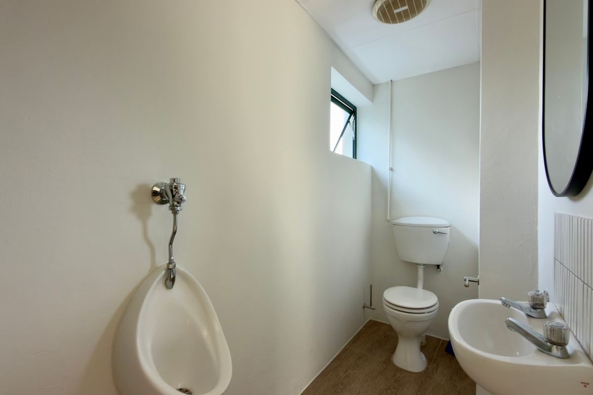 A functional office restroom featuring a wall-mounted urinal, a standard toilet, and a small washbasin with tiled splashback.