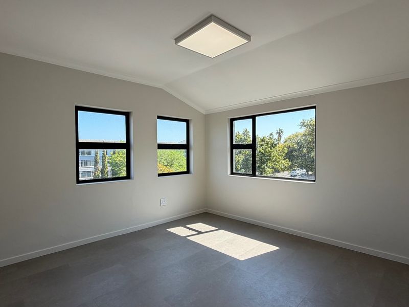 A bright, empty office space featuring modern tiled flooring, neutral walls, and large black-framed windows providing ample natural light.