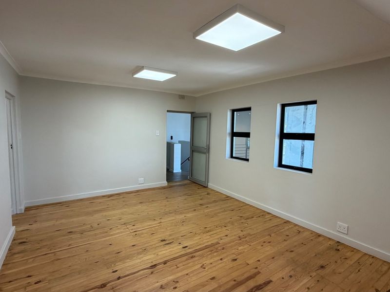 A bright, empty office space featuring polished timber flooring, modern square ceiling light fixtures, and clean white walls.