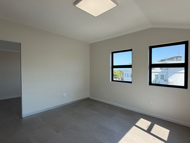 A bright, empty office space featuring modern tiled flooring, neutral walls, and black-framed windows providing natural light.