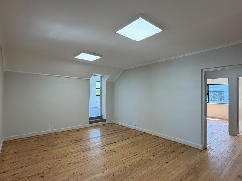 A bright, empty office space featuring polished hardwood flooring, clean white walls, and modern recessed LED panel lighting.