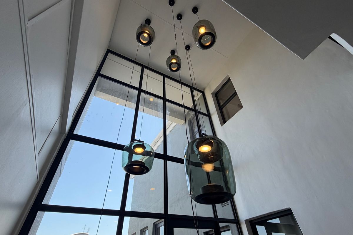 A bright, double-volume entrance area featuring a large steel-framed glass window and modern pendant lighting, creating an airy and welcoming atmosphere.
