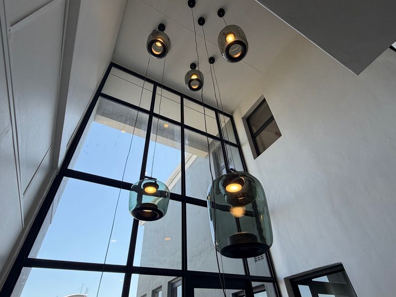 A bright, double-volume entrance area featuring a large steel-framed glass window and modern pendant lighting, creating an airy and welcoming atmosphere.