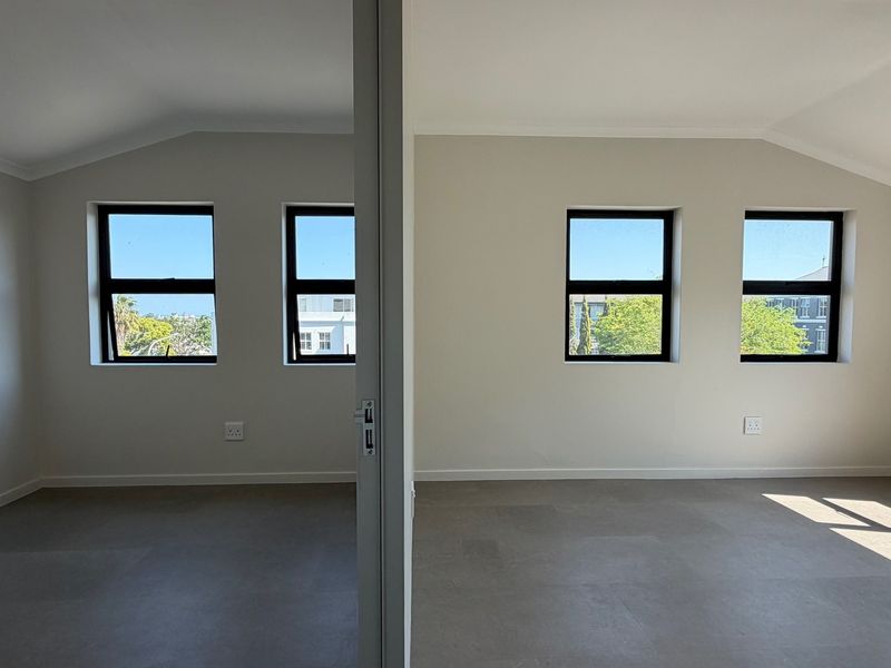 A bright, modern office space featuring neutral walls, tiled flooring, and large black-framed windows providing ample natural light.