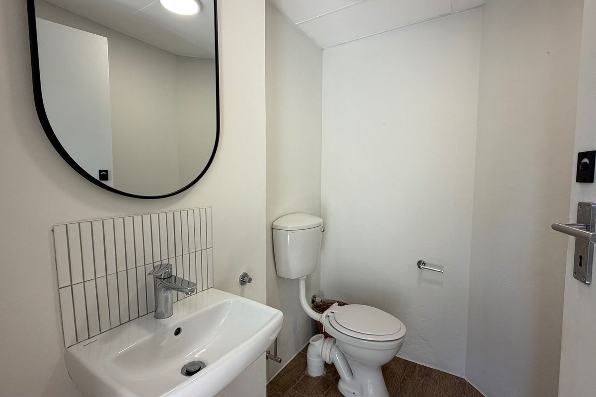 A clean and functional office bathroom featuring a wall-mounted basin with chrome mixer tap, tiled splashback, and a standard toilet.
