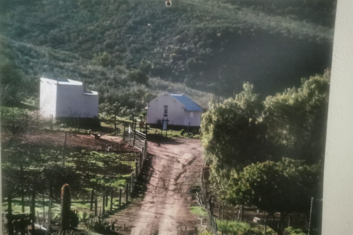 A rural farm property featuring a dirt driveway leading to a main dwelling and an outbuilding, set against a hillside landscape.