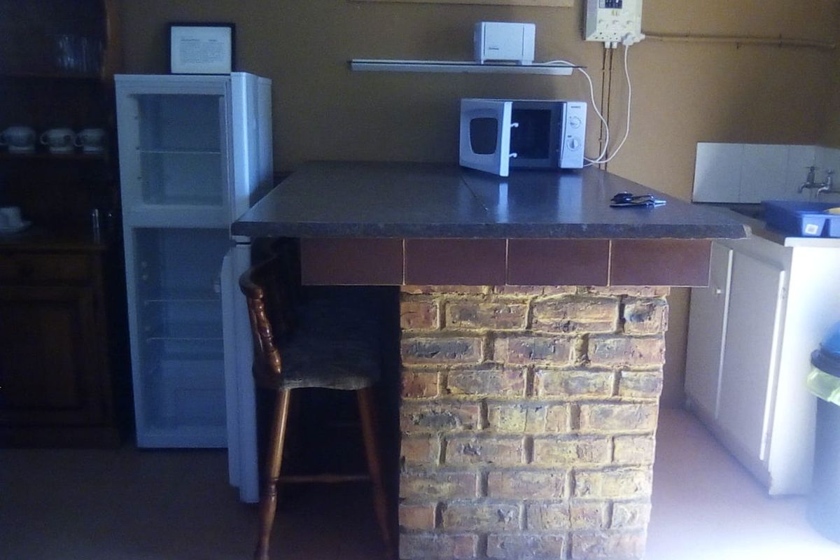 A rustic kitchen area featuring a brick-based breakfast bar with tiled countertop, sink, and basic cabinetry, requiring modernization.