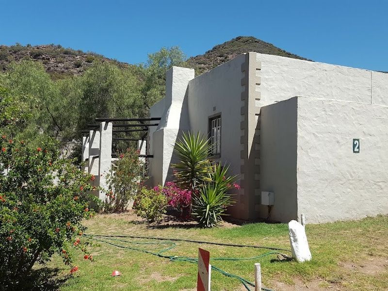 Rear view of a farm-style building featuring textured plaster walls, a masonry chimney, and an attached pergola set against a mountain backdrop.