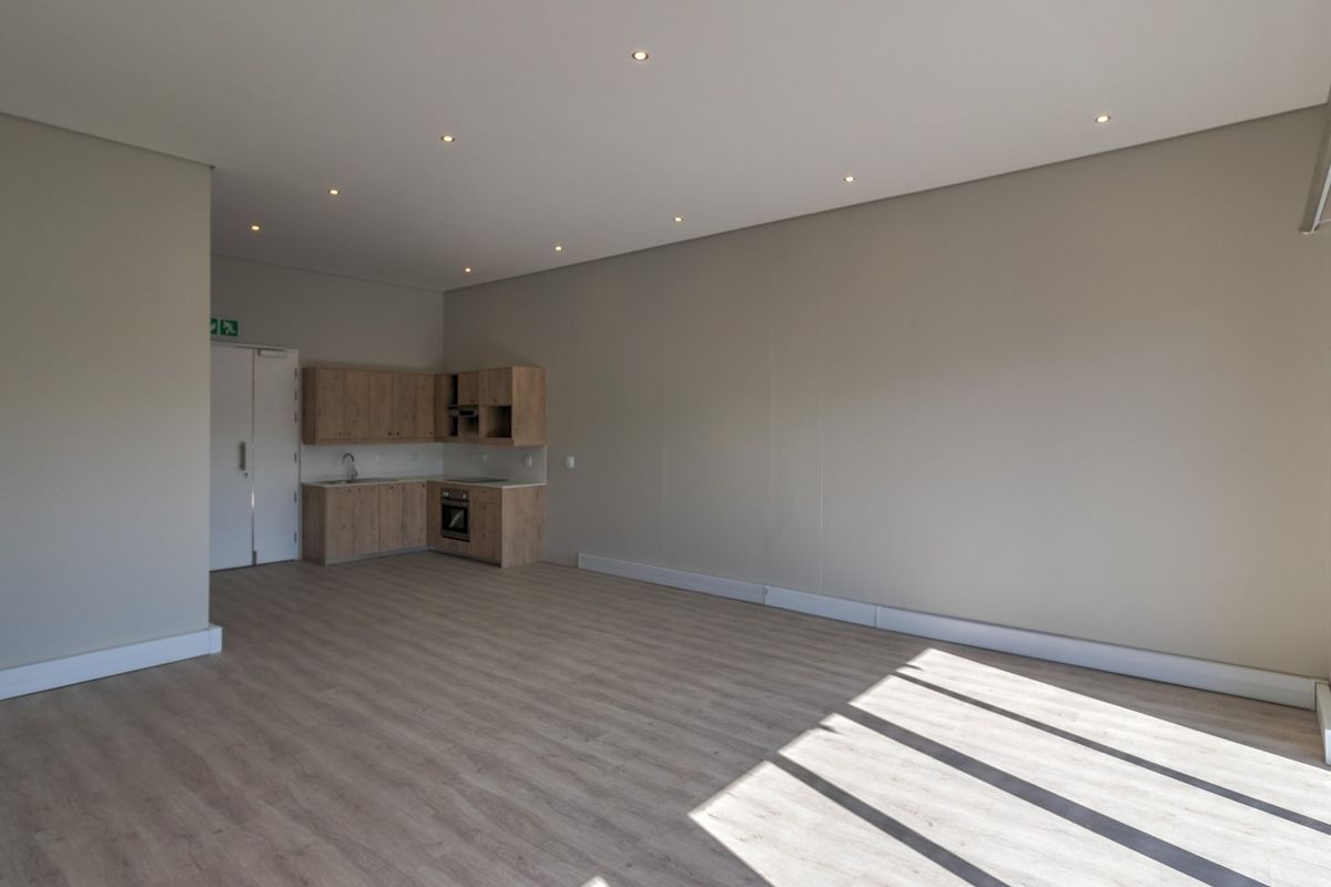 A bright, modern open-plan commercial space featuring light wood-look laminate flooring, recessed lighting, and a compact kitchenette with built-in cabinetry and appliances.